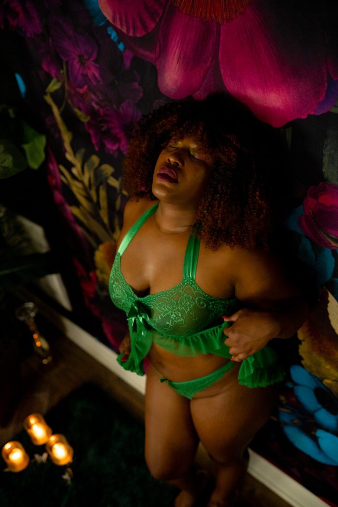 Woman with afro leaning against a floral print wall wearing a green babydoll set