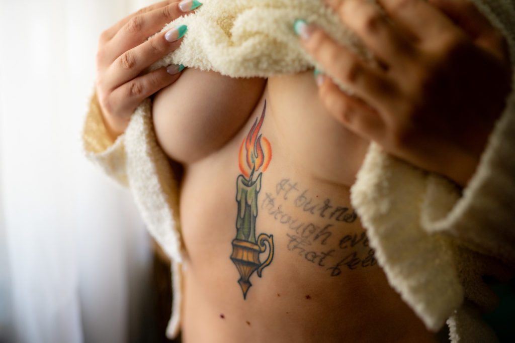 A woman pulling up her sweater to reveal her underboob tattoo