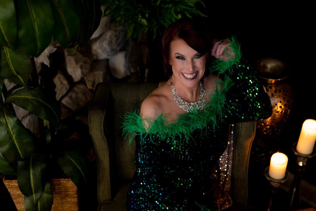 Woman in green sparkly gown, feathers, and diamond necklace smiling